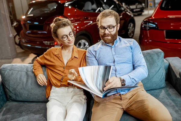 Ζευγάρι με κατάλογο στον καναπέ στην αντιπροσωπεία αυτοκινήτων — Φωτογραφία Αρχείου