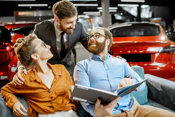 Couple with catalog and sales manager at the car dealership