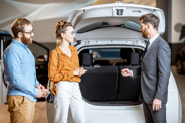 Pareja con gerente de ventas cerca del coche en la sala de exposición — Foto de Stock