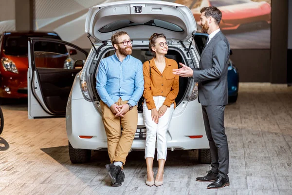 Casal com gerente de vendas perto do carro no showroom — Fotografia de Stock