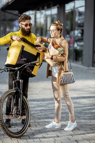 Mensajero entregando comestibles a una joven al aire libre — Foto de Stock