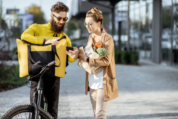 Mensajero entregando comestibles a una joven al aire libre — Foto de Stock