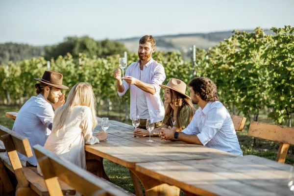 Přátelé popíjejí víno u jídelního stolu na vinici — Stock fotografie