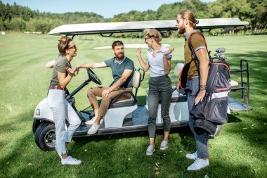 Golf sahasında golf arabasının yanındaki insanlar.