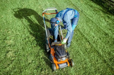 Bahçıvan arka bahçede çim biçme makinesiyle çalışıyor.