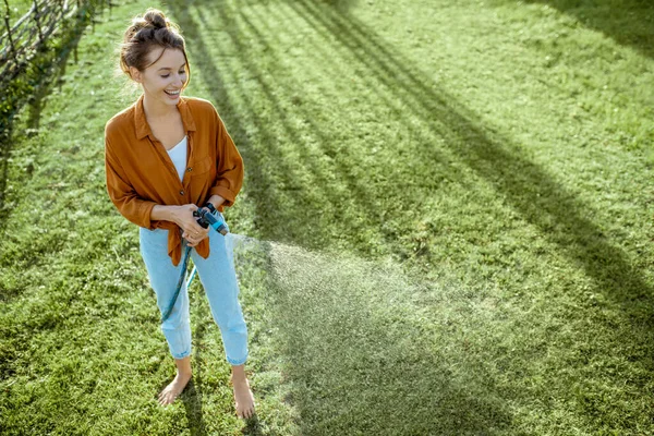 Vrouw water geven groen gazon — Stockfoto