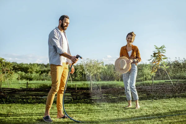 Man en vrouw water geven groen gazon op de achtertuin — Stockfoto