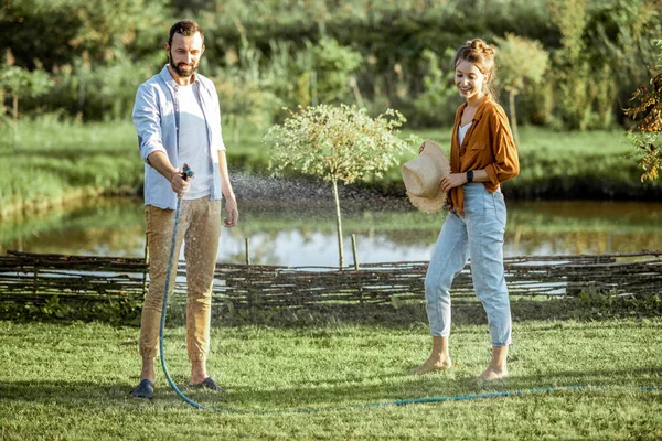 Man and woman watering green lawn on the backyard — Stock Photo, Image