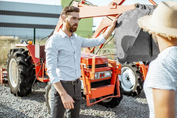 Agronomen med försäljaren nära traktorn i jordbruksbutiken — Stockfoto