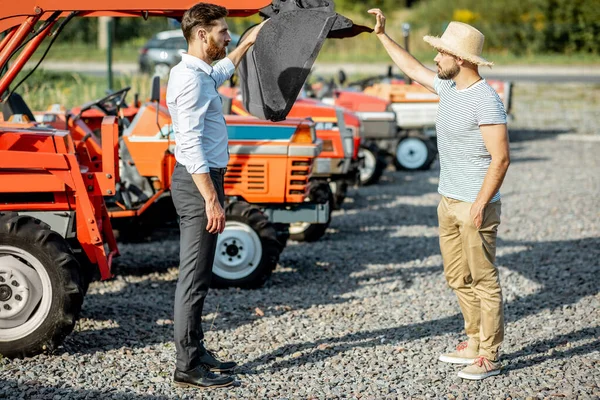 Agrónomo con vendedor cerca de tractor en la tienda agrícola —  Fotos de Stock