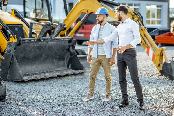 Constructor con un consultor de ventas en la tienda con maquinaria pesada —  Fotos de Stock