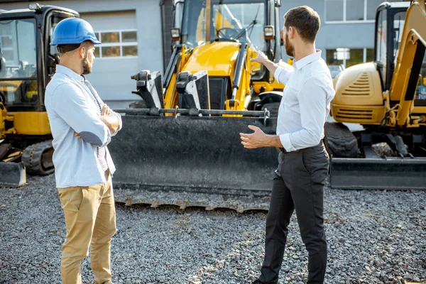 Constructor con un consultor de ventas en la tienda con maquinaria pesada —  Fotos de Stock