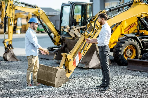 Constructor con un consultor de ventas en la tienda con maquinaria pesada —  Fotos de Stock