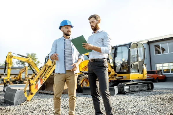 Constructor con un consultor de ventas en la tienda con maquinaria pesada —  Fotos de Stock