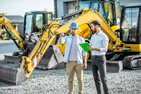 Constructor con un consultor de ventas en la tienda con maquinaria pesada —  Fotos de Stock