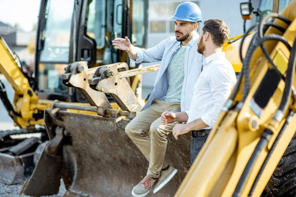 Constructor con un consultor de ventas en la tienda con maquinaria pesada —  Fotos de Stock