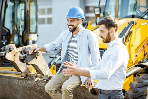 Constructor con un consultor de ventas en la tienda con maquinaria pesada —  Fotos de Stock