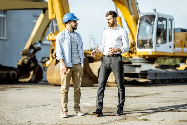 Constructor con un consultor de ventas en la tienda con maquinaria pesada —  Fotos de Stock