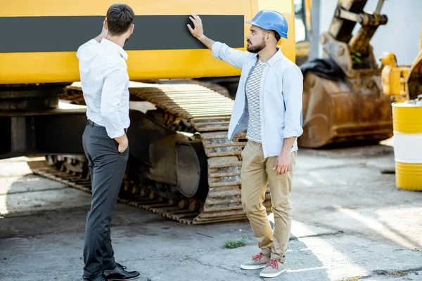 Constructor con un consultor de ventas en la tienda con maquinaria pesada —  Fotos de Stock