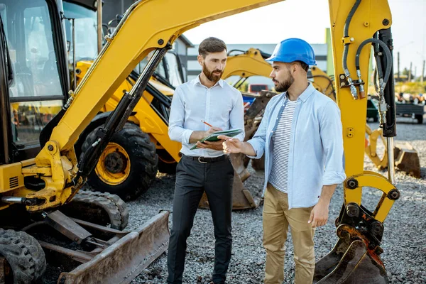 Constructor con un consultor de ventas en la tienda con maquinaria pesada —  Fotos de Stock