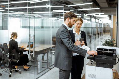 Koridordaki fotokopi makinesinin yanında iş adamları var.
