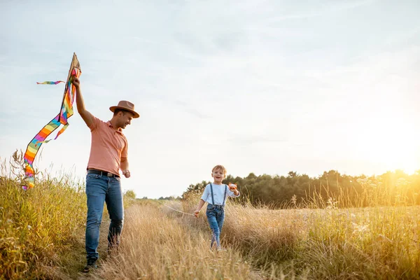 Vader en zoon wandelen met vlieger op het veld — Stockfoto