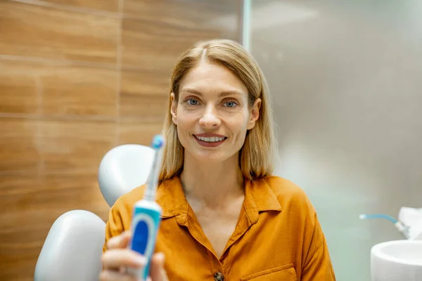 Mujer con cepillo de dientes eléctrico en el consultorio dental —  Fotos de Stock