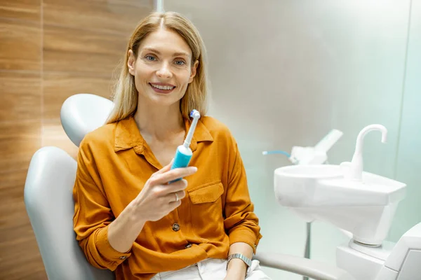 Mulher com escova de dentes elétrica no consultório odontológico — Fotografia de Stock