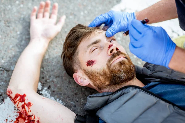 Médico aplicando primeiros socorros para a pessoa sangrando na estrada — Fotografia de Stock