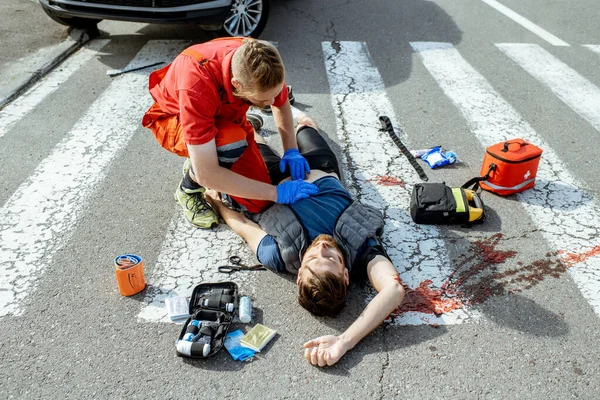 Médico aplicando atendimento de emergência para o homem ferido na estrada — Fotografia de Stock