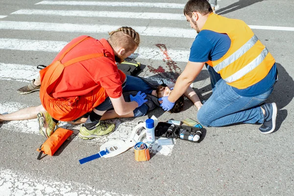 Médicos que aplican atención de emergencia al hombre herido en la carretera —  Fotos de Stock