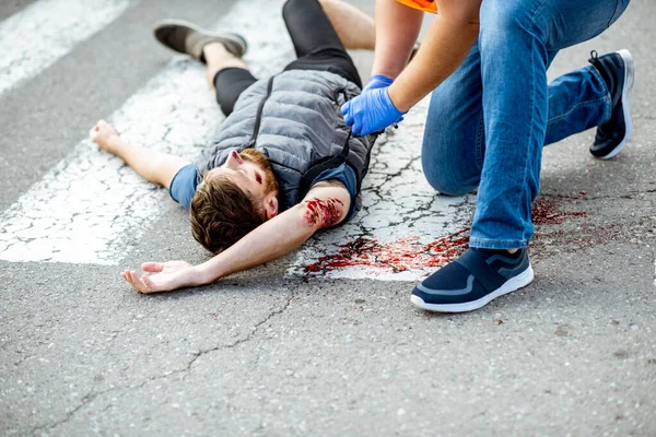 Az az ember, aki elsősegélyt nyújt a vérző személynek az úton — Stock Fotó