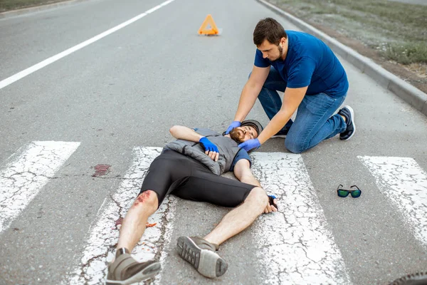 Acidente de viação com ciclista ferido e homem que presta primeiros socorros — Fotografia de Stock