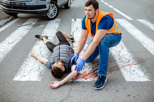 Mężczyzna stosujący pierwszą pomoc u krwawiącej osoby na drodze — Zdjęcie stockowe