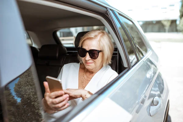 Starší žena s telefonem v autě — Stock fotografie
