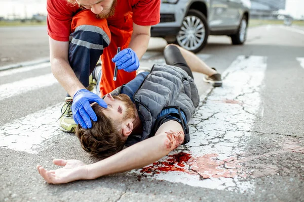 Médico aplicando primeros auxilios a la persona sangrante en la carretera —  Fotos de Stock