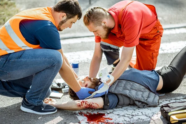 Medics applying emergency care to the injured man on the road — Stock Photo, Image