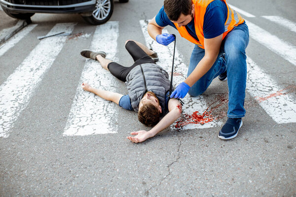 Человек, который оказывает первую помощь кровоточащему человеку на дороге
