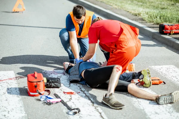 Médicos que aplican atención de emergencia al hombre herido en la carretera —  Fotos de Stock