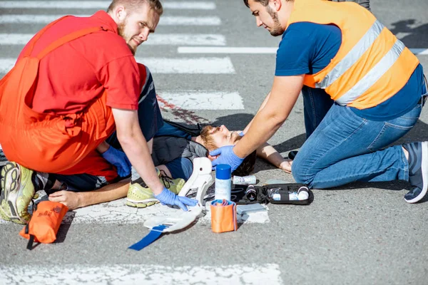 Médicos que aplican atención de emergencia al hombre herido en la carretera —  Fotos de Stock