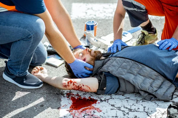 Medics applying emergency care to the injured man on the road — Stock Photo, Image