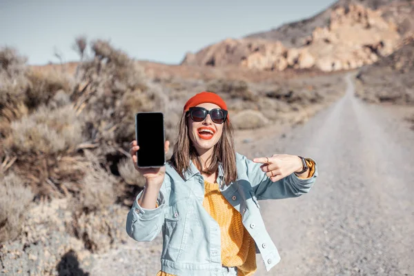 Женщина со смартфоном путешествует по пустынной дороге — стоковое фото