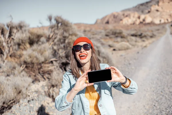 Женщина со смартфоном путешествует по пустынной дороге — стоковое фото