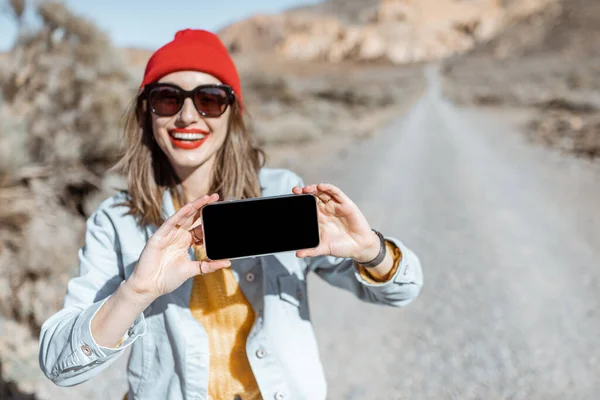 Mujer con teléfono inteligente que viaja por el camino del desierto —  Fotos de Stock