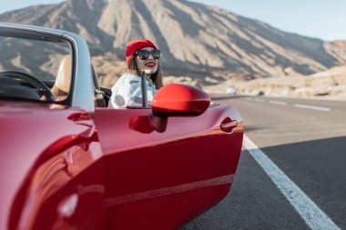 Woman traveling by the red car on a desert road