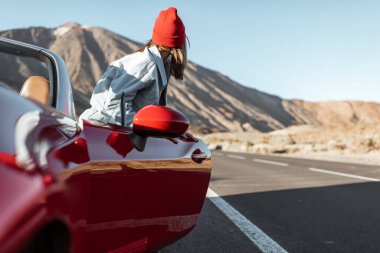 Woman traveling by the red car on a desert road