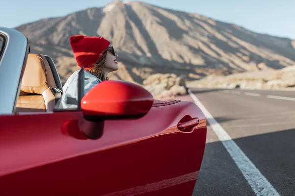 Woman traveling by the red car on a desert road — Stock fotografie