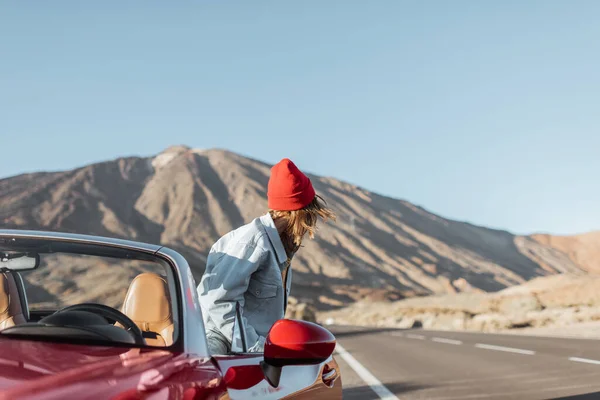 Woman traveling by the red car on a desert road — Φωτογραφία Αρχείου