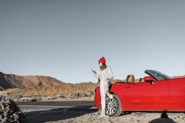 Woman traveling by the red car on a desert road — Zdjęcie stockowe