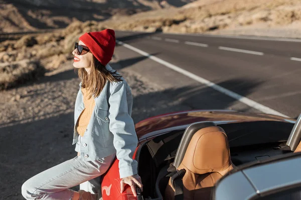 Жінка подорожує червоною машиною на пустельній дорозі — стокове фото